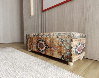 Puede incluir: Un otomán rectangular con una tela estampada en tonos naranja, azul y rojo. El diseño presenta motivos geométricos y florales. El otomán se asienta sobre cuatro patas de madera cortas, redondeadas y de color claro. El estilo general recuerda a una alfombra vintage.