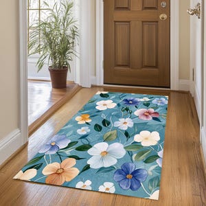 May include: A blue floral area rug with a watercolor design featuring pink, white, yellow, and blue flowers. The rug is placed in a hallway with a wooden floor.