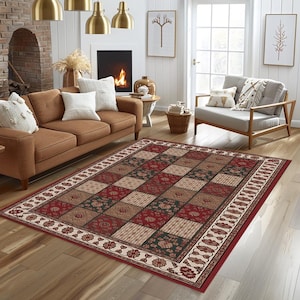 May include: A patterned rectangular rug in a living room setting. The rug features a repeating square design in red, beige, and green, with floral and textured elements. It has a floral and scroll border. The rug is placed on a wooden floor.
