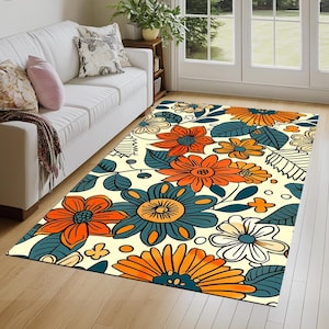 May include: A rectangular area rug with a floral pattern. The rug features large orange, teal, and white flowers with green leaves against a cream background. The rug is placed on a hardwood floor near a white sofa.