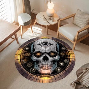 Puede incluir: Una alfombra circular que presenta un cráneo gris central con un tercer ojo en la frente y ojos de color naranja brillante. El diseño incluye un borde circular oscuro con patrones de cuadrícula geométrica y varios símbolos blancos pequeños.