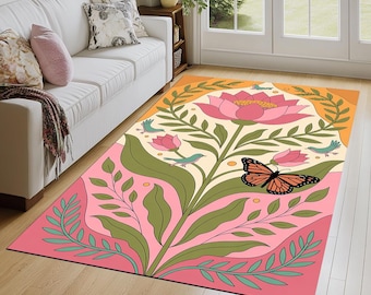 May include: A rectangular area rug featuring a central large pink lotus flower, smaller pink buds, green leafy stems, small teal birds, and a monarch butterfly with orange and black wings, set against a cream, pink, and orange background.