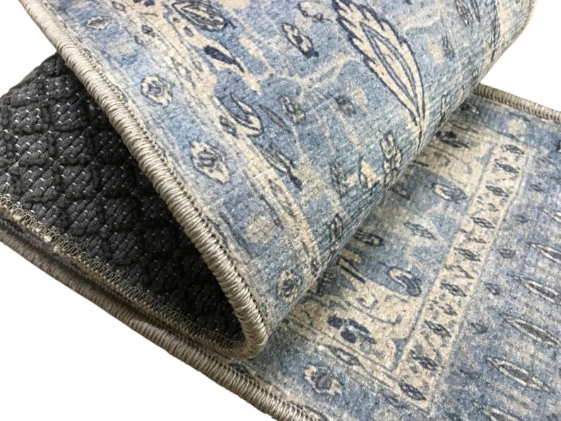 a close-up view of a blue and white patterned rug or carpet, with a black and gray geometric patterned mat or rug visible underneath it.