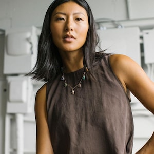 Puede incluir: Una blusa sin mangas de color marr&oacute;n oscuro con cuello alto combinada con un delicado collar de cadena dorada que presenta peque&ntilde;os colgantes de piedras preciosas de formas irregulares en tonos morado, verde y rosa.
