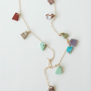Puede incluir: Un collar de cadena fina en tono dorado con un surtido de peque&ntilde;os dijes de piedra de formas irregulares y multicolores. Los dijes incluyen tonos turquesa, rojo, marr&oacute;n, blanco, verde y morado, espaciados uniformemente por los eslabones.