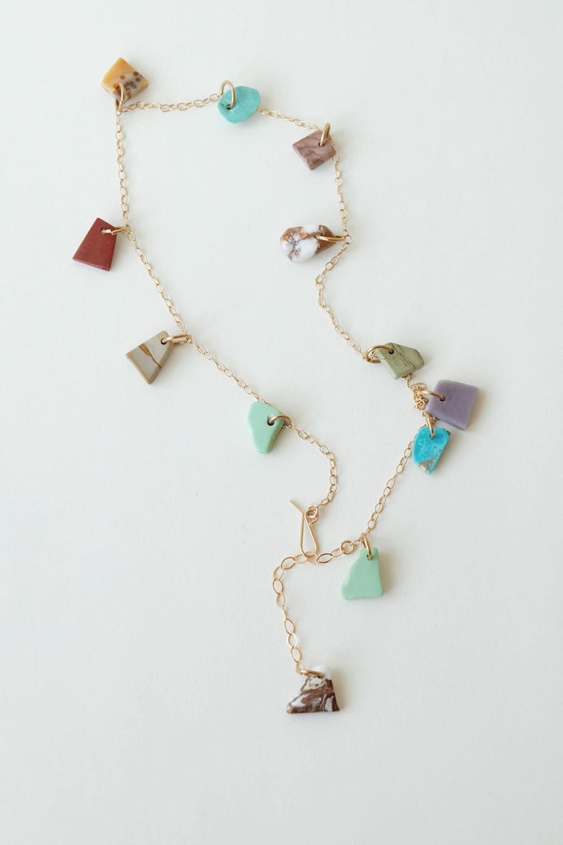 Puede incluir: Un collar de cadena fina en tono dorado con un surtido de peque&ntilde;os dijes de piedra de formas irregulares y multicolores. Los dijes incluyen tonos turquesa, rojo, marr&oacute;n, blanco, verde y morado, espaciados uniformemente por los eslabones.