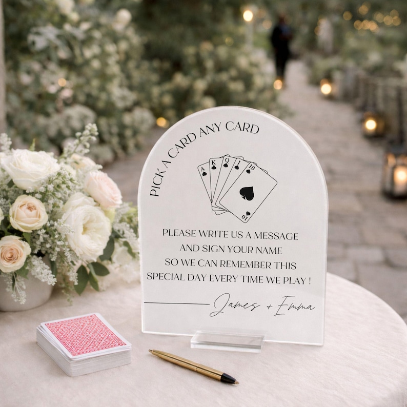 May include: An arched clear acrylic sign with black text reading PICK A CARD ANY CARD, PLEASE WRITE US A MESSAGE AND SIGN YOUR NAME SO WE CAN REMEMBER THIS SPECIAL DAY EVERY TIME WE PLAY!, and James + Emma, featuring a playing card graphic.