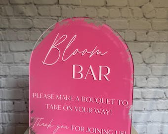 May include: A pink acrylic Bloom Bar sign with white lettering. The sign has an arched top and includes the phrases "PLEASE MAKE A BOUQUET TO TAKE ON YOUR WAY!" and "Thank you FOR JOINING US!"