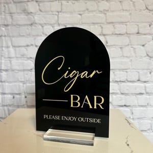 May include: Black acrylic sign with gold lettering that reads "Cigar Bar - Please Enjoy Outside".