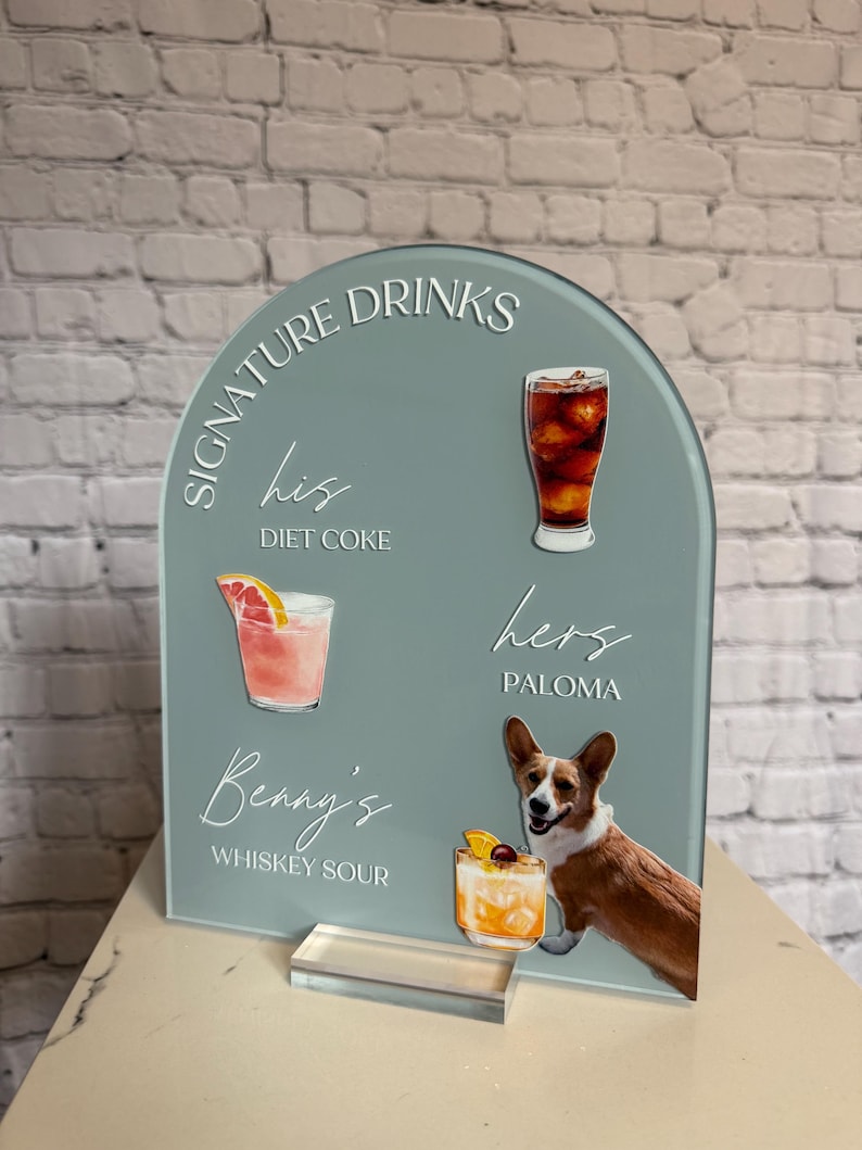 May include: A teal acrylic drinks sign with the words "Signature Drinks" and drink illustrations. The sign includes the text "his Diet Coke", "hers Paloma", and "Benny's Whiskey Sour". A corgi dog is featured on the sign.