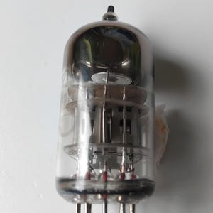 Puede incluir: Un tubo de vacío de vidrio transparente con una estructura interna plateada y una parte superior negra. El tubo tiene múltiples pines en la base y está diseñado para aplicaciones electrónicas.