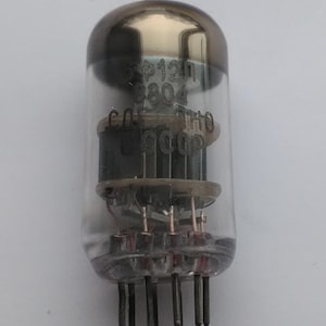 Peut inclure: Un tube à vide vintage avec un corps en verre transparent et un dessus argenté. Le tube comporte plusieurs composants internes et une série de broches à la base. Le texte "ФР12П" et d'autres marquages sont visibles sur le verre.