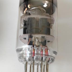 May include: A clear glass valve with a dark, metallic top and multiple pins at the base. The internal components are visible, including a central structure and several smaller elements with red and silver accents.