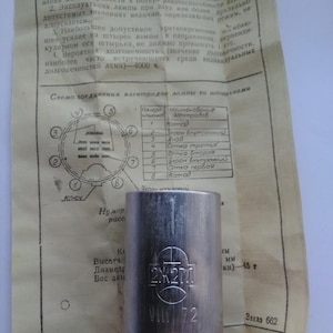 May include: A silver-colored vacuum tube with the text "2K270" and "VII 72" printed on it. The tube is cylindrical with a flared base and several pins. A paper with technical diagrams and Russian text is in the background.