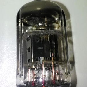 Puede incluir: Un tubo de vacío de vidrio transparente con una base de metal negro y varios cables de cobre. El tubo tiene una parte superior plateada y un componente de metal negro en el interior.