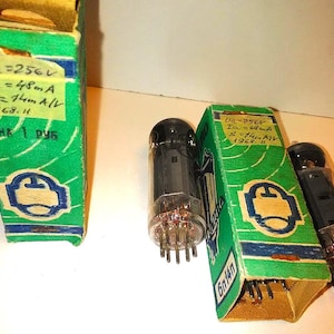 Puede incluir: Válvulas de vacío vintage con carcasas de vidrio y clavijas metálicas, presentadas con sus cajas originales verdes y amarillas. Las cajas tienen especificaciones técnicas manuscritas y el texto "ЦЕНА 1 РУБ".