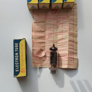 May include: Five blue and yellow boxes with the text "Electron Tube" and the logo "V/O Electronorgtechnica" printed on them. A glass vacuum tube with a metal base and six pins is sitting on a brown paper with text in Russian.
