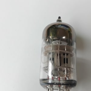 Op de afbeelding: Een vintage vacuümbuis met een heldere glazen behuizing en een zilverkleurige bovenkant. De interne componenten, waaronder draadfilamenten en ondersteunende structuren, zijn zichtbaar. De buis heeft meerdere pinnen aan de basis voor elektrische aansluitingen.