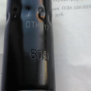 May include: A black cylindrical metal object with the text "OTK 17" and "679" embossed on its surface. The object has a glossy finish and appears to be a component or part of a larger mechanism.