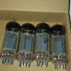 May include: Four vacuum tubes labeled 6P41S, marked as NOS (new), inside a cardboard box. Each tube has a glass enclosure, a dark top, and a gray internal structure with visible pins. The box has handwritten text.