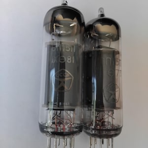 May include: A white ceramic mug with a black handle and the text "But First, Coffee" in a bold, black font. The mug is set against a blurred background, suggesting a cozy setting.