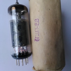 Op de afbeelding: Een glazen vacuümbuis met een zwarte metalen basis en een bruine papieren buis met de tekst "6H13-EB" erop gedrukt.