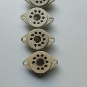 Może przedstawiać: Pionowe ułożenie pięciu gniazd lamp próżniowych w stylu vintage. Każde gniazdo jest w kolorze złamanej bieli, z centralnym okrągłym otworem otoczonym mniejszymi otworami. Posiadają uchwyty montażowe po obu stronach.