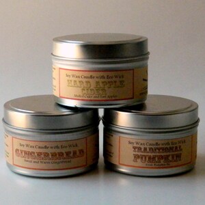 May include: Three silver candle tins with labels. The labels are brown with gold text. The candles are labeled "Hard Apple Cider", "Gingerbread", and "Traditional Pumpkin".