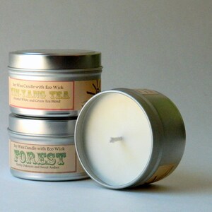 May include: Three soy wax candles in silver tins with labels. The top candle is labeled "In-Yang Tea" with the text "Blend White and Green Tea Blend". The middle candle is labeled "Forest" with the text "Earthy Oakmoss and Sweet Amber".