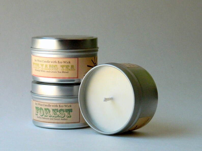 May include: Three soy wax candles in silver tins with labels. The top candle is labeled "In-Yang Tea" with the text "Blend White and Green Tea Blend". The middle candle is labeled "Forest" with the text "Earthy Oakmoss and Sweet Amber".