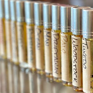 May include: A row of small, silver roll-on bottles with labels that read "Tuxedo", "Woodstock", "Palo", "Drift Away", "Nu", "Oreo", "Panama", and "Lavender".