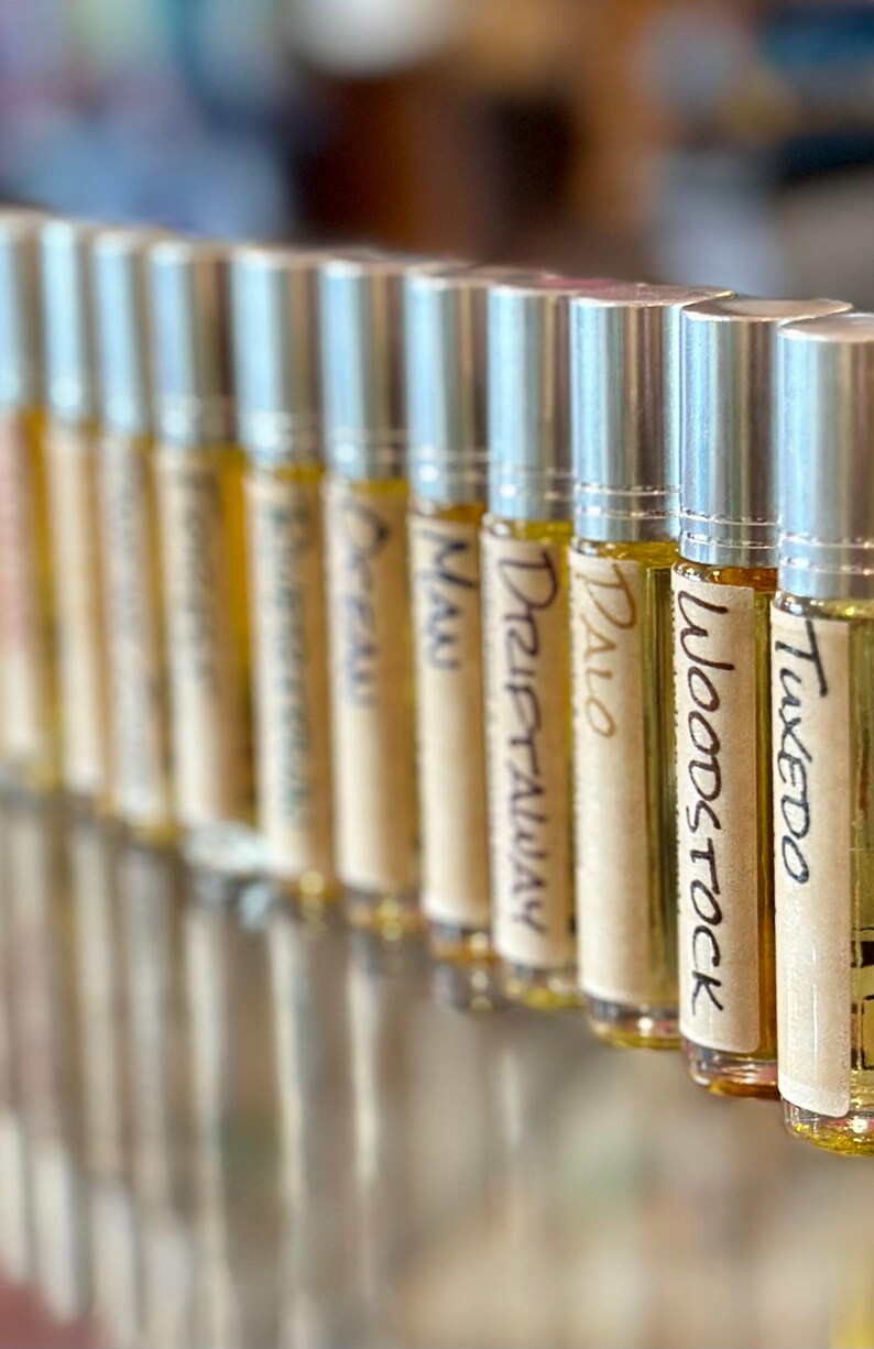 May include: A row of small, silver roll-on bottles with labels that read "Tuxedo", "Woodstock", "Palo", "Drift Away", "Nu", "Oreo", "Panama", and "Lavender".