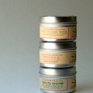 May include: Three silver candle tins with labels. The top tin has a label that says "Soy Wax Candle with Eco Wick Yin-Yang Tea Oriental White and Green Tea Blend". The middle tin has a label that says "Soy Wax Candle with Eco Wick Utopia Soft. Heavenly Floral". The bottom tin has a label that says "Soy Wax Candle with Eco Wick Forest Earthy Oakmoss and Sweet Amber".