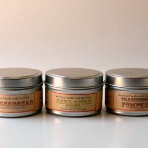 May include: Three silver candle tins with labels. The labels are orange and brown with white text. The labels read "Soy Wax Candle with Eco Wick" and the scents are "Gingerbread", "Hard Apple Cider", and "Traditional Pumpkin".
