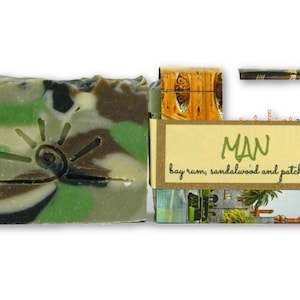 May include: A bar of soap with a camouflage pattern and a sun design. The soap is labelled "MAN bay rum, sandalwood and patchouli".