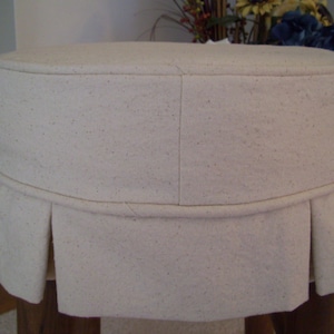 Peut inclure: Un tabouret en tissu blanc avec une jupe pliss&eacute;e. Le tabouret est fait d'un tissu doux et textur&eacute; et a un design simple et &eacute;l&eacute;gant.