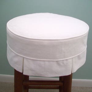 Peut inclure: Housse de tabouret ronde blanche avec un volant pliss&eacute; autour du bord inf&eacute;rieur. La housse est faite d'un tissu blanc doux et est con&ccedil;ue pour s'adapter &agrave; un tabouret rond.