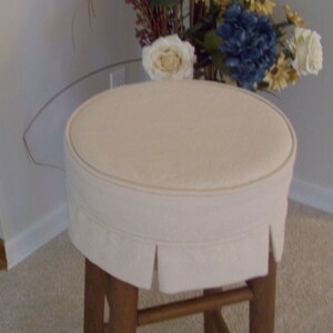 Peut inclure: Un tabouret ovale blanc avec une base en bois. Le tabouret a une jupe en tissu pliss&eacute;e et est recouvert d'un tissu de couleur cr&egrave;me.