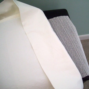 May include: A close-up of a cream-colored fabric, possibly linen or cotton, draped over a black and white patterned surface. The fabric has a smooth texture and is folded over, revealing its interior. The background is a muted green wall.