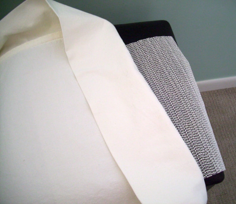May include: A close-up of a cream-colored fabric, possibly linen or cotton, draped over a black and white patterned surface. The fabric has a smooth texture and is folded over, revealing its interior. The background is a muted green wall.