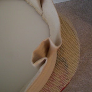 Peut inclure: Gros plan sur un tissu beige recouvrant un objet rond. Le tissu est pli&eacute; et pr&eacute;sente une texture tiss&eacute;e. L'objet est partiellement visible sous le tissu.