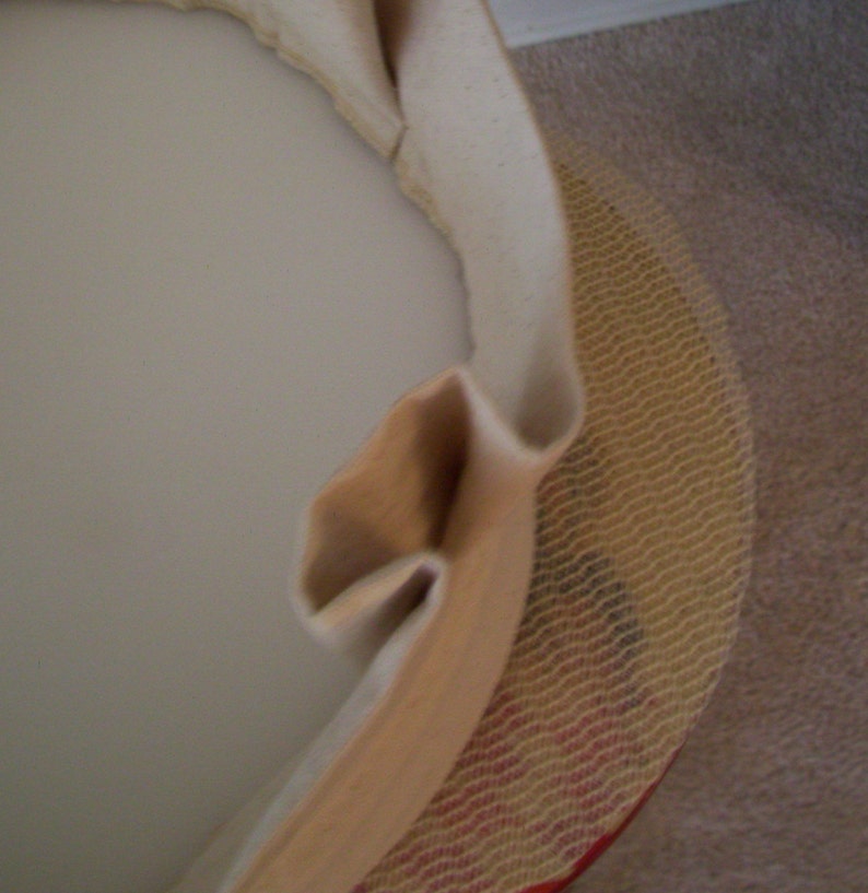 Peut inclure: Gros plan sur un tissu beige recouvrant un objet rond. Le tissu est pli&eacute; et pr&eacute;sente une texture tiss&eacute;e. L'objet est partiellement visible sous le tissu.
