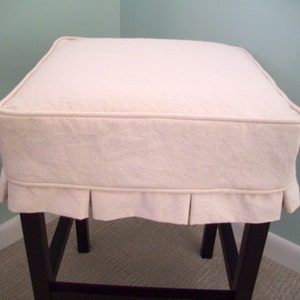 May include: A white fabric chair cushion with a pleated ruffle around the bottom edge. The cushion is on top of a dark brown wooden chair.
