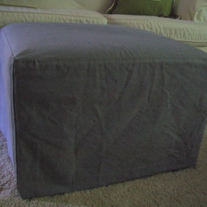 Pu&ograve; includere: Un pouf quadrato in tessuto grigio con una superficie liscia e testurizzata.