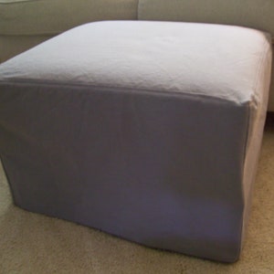 May include: A light gray fabric ottoman with a square shape and a smooth, flat top.