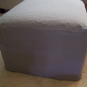 Pu&ograve; includere: Un pouf quadrato in tessuto grigio con un piano superiore liscio e piatto.