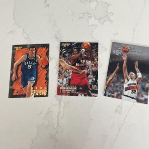 May include: Three basketball trading cards featuring NBA players. The cards display action shots of Jason Kidd, Dikembe Mutombo, and a player wearing a Dallas Mavericks jersey with the number 5. The cards are from the Fleer and Skybox brands.