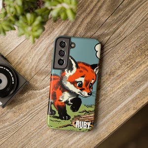 May include: A phone case with a cartoon fox illustration in red, orange, and white. The fox is looking down with a blue background and the word "RUBY" in white text at the bottom.