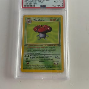 Puede incluir: Una carta Holo de Vileplume de 1999 de Pok&eacute;mon Jungle. La carta presenta una ilustraci&oacute;n de Vileplume con una cabeza roja y morada en forma de flor. La carta est&aacute; calificada como NM-MT 8 y es una 1&ordf; edici&oacute;n.
