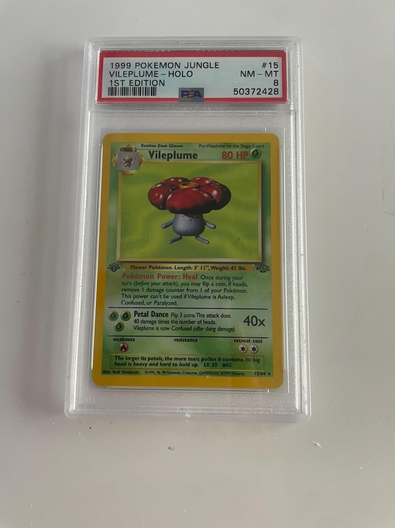 Puede incluir: Una carta Holo de Vileplume de 1999 de Pok&eacute;mon Jungle. La carta presenta una ilustraci&oacute;n de Vileplume con una cabeza roja y morada en forma de flor. La carta est&aacute; calificada como NM-MT 8 y es una 1&ordf; edici&oacute;n.
